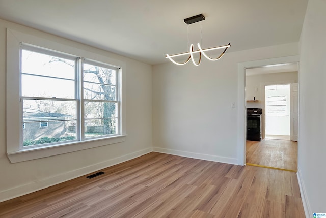 spare room with a chandelier, light hardwood / wood-style flooring, and a healthy amount of sunlight