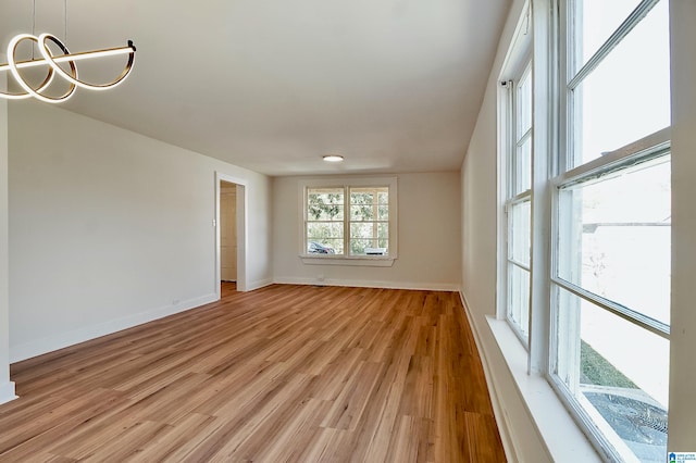 unfurnished room with a chandelier and light wood-type flooring