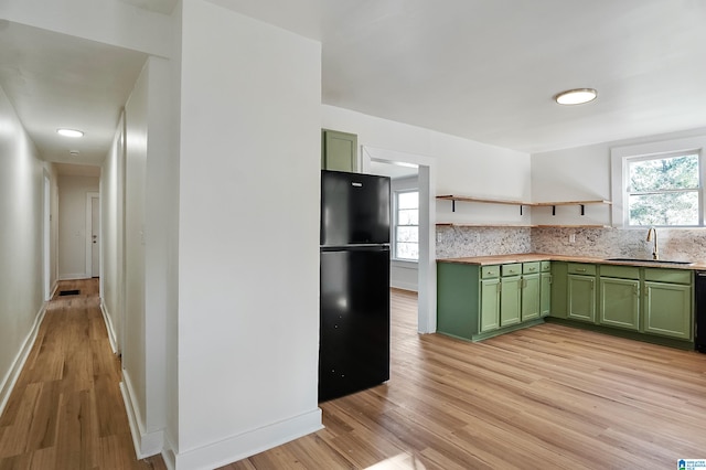 kitchen featuring green cabinets, black fridge, light hardwood / wood-style floors, and sink