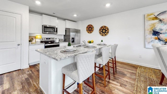 kitchen featuring dark hardwood / wood-style flooring, stainless steel appliances, a kitchen island with sink, white cabinetry, and a breakfast bar area