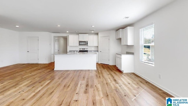 kitchen featuring a kitchen island with sink, range with electric cooktop, light stone countertops, light hardwood / wood-style floors, and white cabinetry