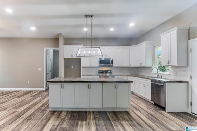 kitchen featuring a center island, appliances with stainless steel finishes, pendant lighting, white cabinets, and hardwood / wood-style flooring