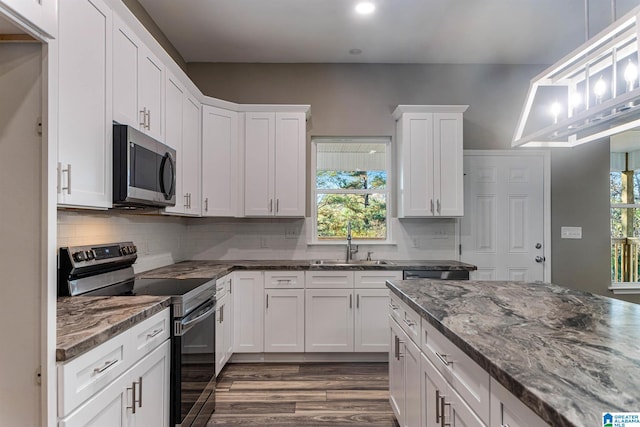 kitchen with stainless steel appliances, white cabinetry, a wealth of natural light, and dark stone counters