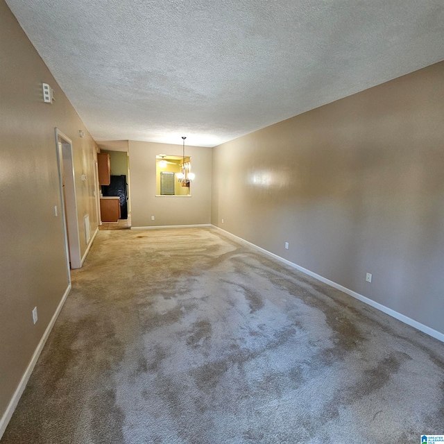 carpeted spare room with a chandelier and a textured ceiling