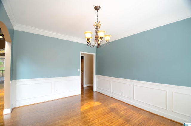 spare room featuring wood-type flooring, ornamental molding, and a chandelier