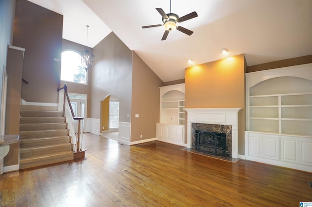 unfurnished living room featuring built in shelves, wood-type flooring, ceiling fan with notable chandelier, and high vaulted ceiling