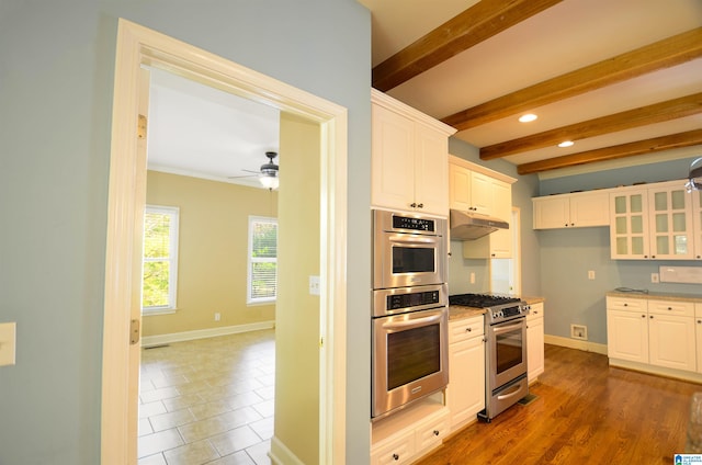 kitchen featuring appliances with stainless steel finishes, ceiling fan, beam ceiling, dark tile patterned flooring, and white cabinetry