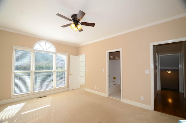 unfurnished bedroom featuring ensuite bath, ornamental molding, light colored carpet, ceiling fan, and a spacious closet