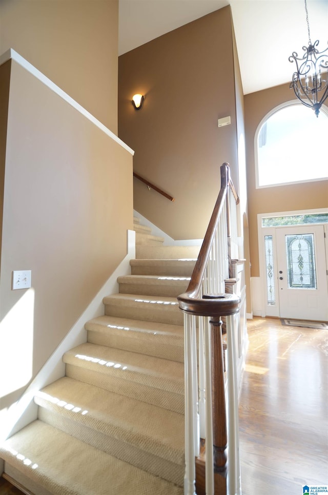 stairs with high vaulted ceiling, wood-type flooring, and a notable chandelier