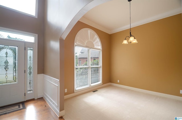 foyer with light hardwood / wood-style floors, ornamental molding, and an inviting chandelier