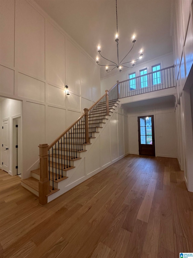 unfurnished living room with hardwood / wood-style floors, ornamental molding, a high ceiling, and a notable chandelier