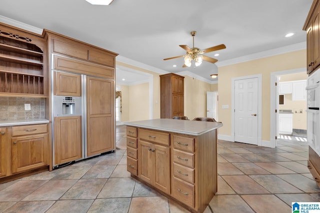 kitchen with ceiling fan, a center island, backsplash, paneled built in fridge, and ornamental molding