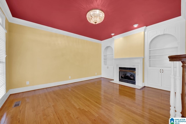 unfurnished living room with hardwood / wood-style flooring, built in shelves, a fireplace, and crown molding