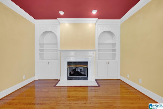 unfurnished living room with hardwood / wood-style floors, built in shelves, crown molding, and a high end fireplace