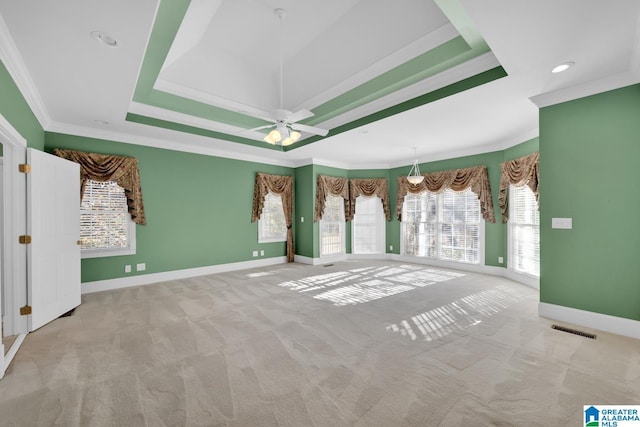 carpeted empty room featuring a tray ceiling, a wealth of natural light, ceiling fan, and ornamental molding