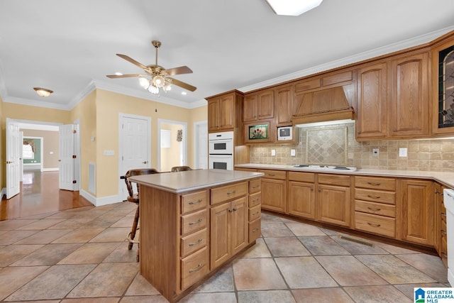 kitchen featuring white appliances, premium range hood, crown molding, decorative backsplash, and a kitchen island