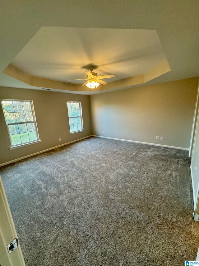 unfurnished room with dark carpet, a raised ceiling, and ceiling fan