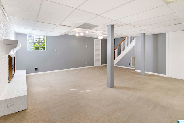 basement featuring carpet floors, a brick fireplace, and a drop ceiling