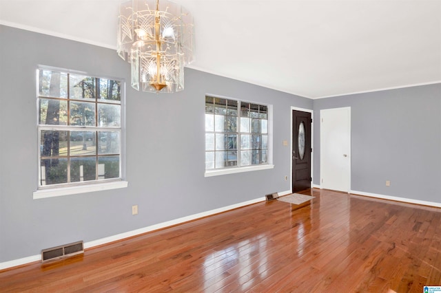 unfurnished room with hardwood / wood-style flooring, a healthy amount of sunlight, crown molding, and a chandelier