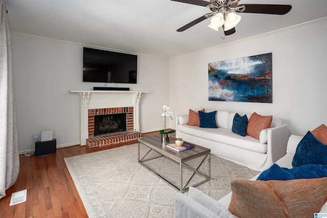 living room with hardwood / wood-style floors, crown molding, a brick fireplace, ceiling fan, and a textured ceiling