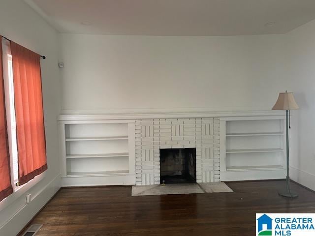 unfurnished living room with a fireplace, built in features, and dark wood-type flooring