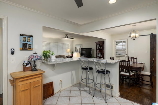 kitchen featuring ceiling fan, hanging light fixtures, a barn door, kitchen peninsula, and a breakfast bar area