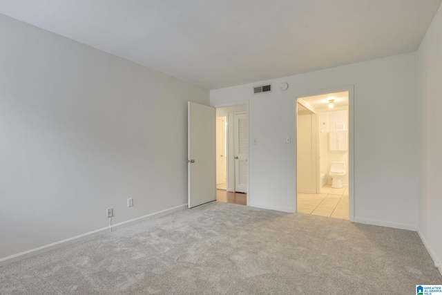 unfurnished bedroom with ensuite bathroom and light colored carpet