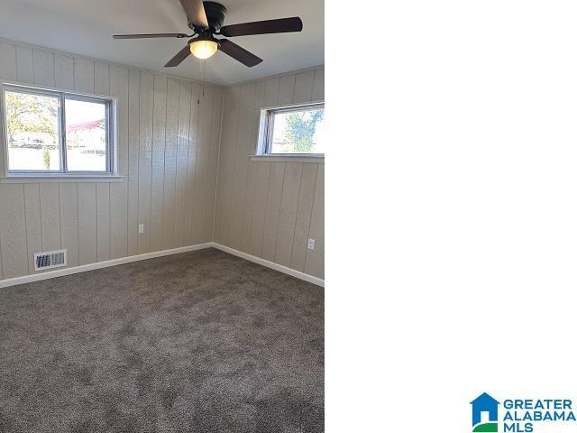 carpeted spare room with a wealth of natural light, wooden walls, and ceiling fan