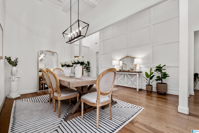 dining area with ornamental molding, beam ceiling, an inviting chandelier, a high ceiling, and light hardwood / wood-style floors