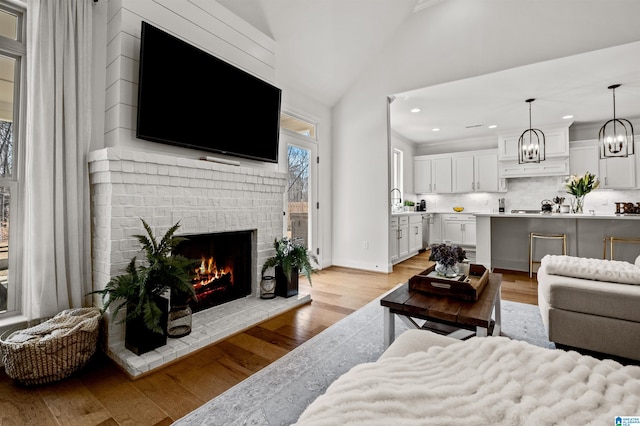 living room featuring high vaulted ceiling, crown molding, sink, a brick fireplace, and light wood-type flooring