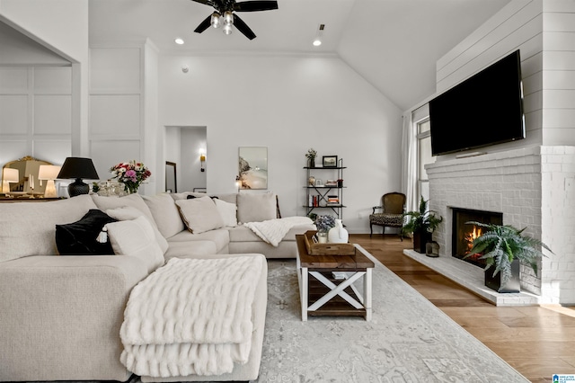 living room featuring hardwood / wood-style floors, high vaulted ceiling, crown molding, ceiling fan, and a fireplace