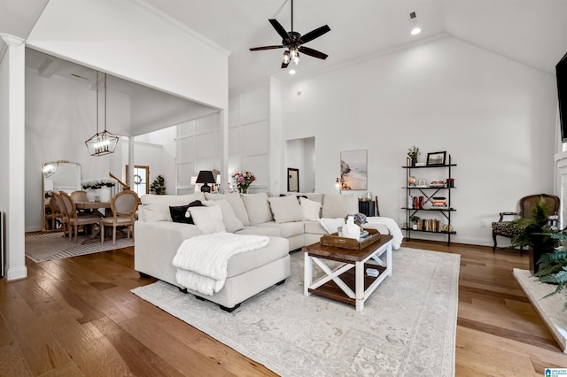 living room featuring hardwood / wood-style floors, ceiling fan with notable chandelier, high vaulted ceiling, and crown molding