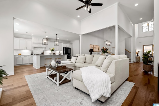 living room with ceiling fan, light wood-type flooring, ornamental molding, and a high ceiling