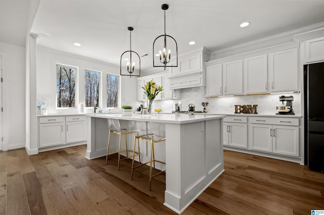 kitchen with tasteful backsplash, white cabinetry, a center island with sink, and wood-type flooring