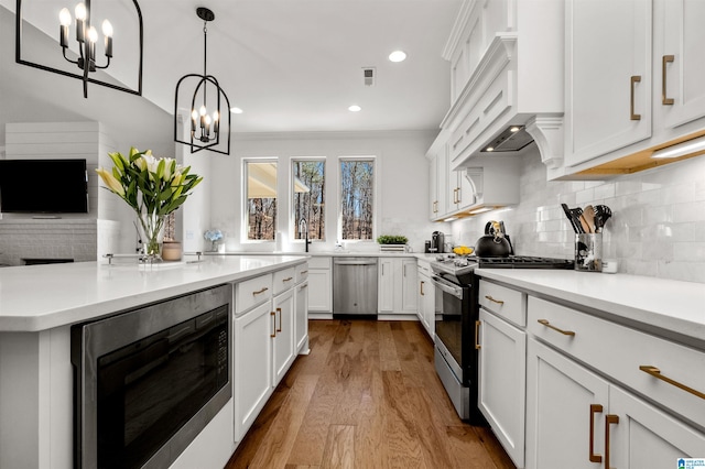 kitchen with pendant lighting, white cabinets, crown molding, hardwood / wood-style flooring, and appliances with stainless steel finishes