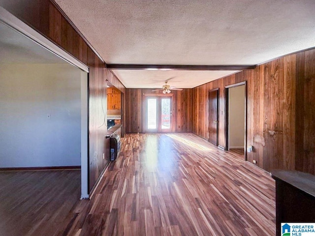 unfurnished living room with ceiling fan, french doors, wood-type flooring, a textured ceiling, and wooden walls