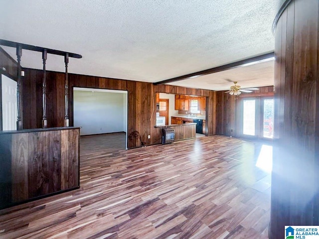 unfurnished living room featuring hardwood / wood-style floors, a textured ceiling, ceiling fan, and wood walls