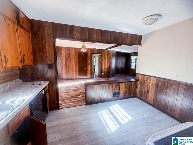 kitchen featuring light wood-type flooring, ceiling fan, sink, black dishwasher, and wood walls