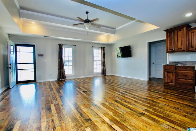 unfurnished living room with ceiling fan, a raised ceiling, dark wood-type flooring, and crown molding