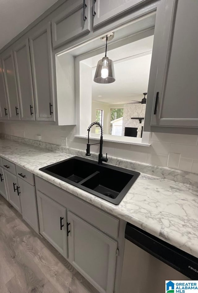 kitchen featuring gray cabinetry, dishwasher, sink, light stone counters, and light hardwood / wood-style floors