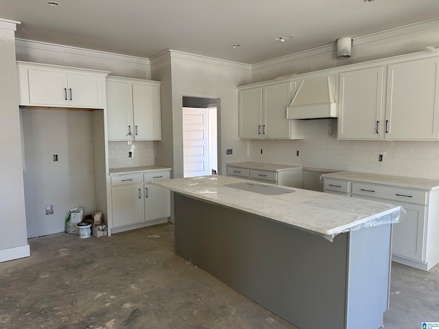 kitchen with white cabinetry, light stone countertops, tasteful backsplash, a kitchen island, and custom range hood