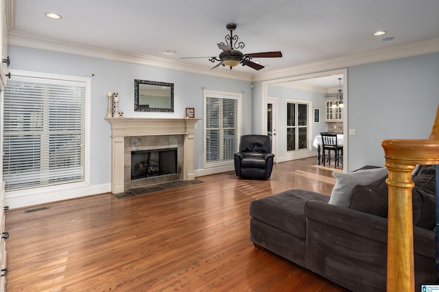 living room with hardwood / wood-style floors, ceiling fan with notable chandelier, crown molding, and a tiled fireplace