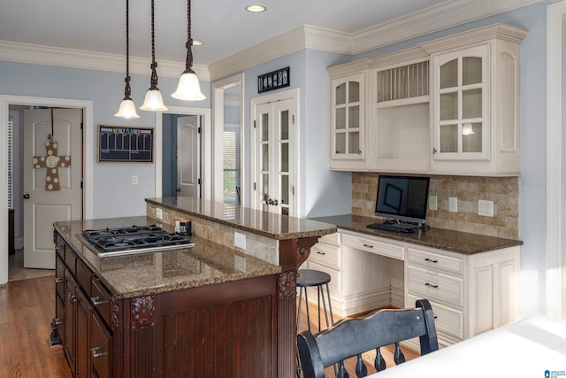 kitchen featuring a center island, dark wood-type flooring, hanging light fixtures, stainless steel gas stovetop, and a breakfast bar