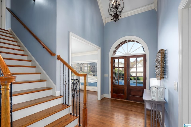 foyer with a high ceiling, french doors, crown molding, dark hardwood / wood-style flooring, and a chandelier