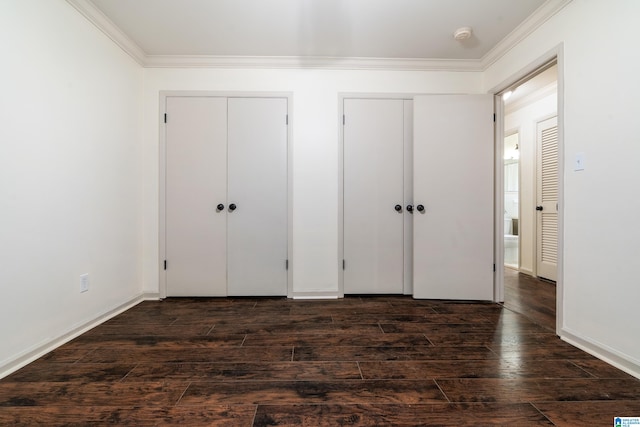 unfurnished bedroom featuring ornamental molding, dark hardwood / wood-style flooring, and multiple closets