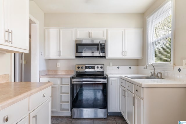 kitchen with white cabinets, appliances with stainless steel finishes, dark tile patterned flooring, and sink