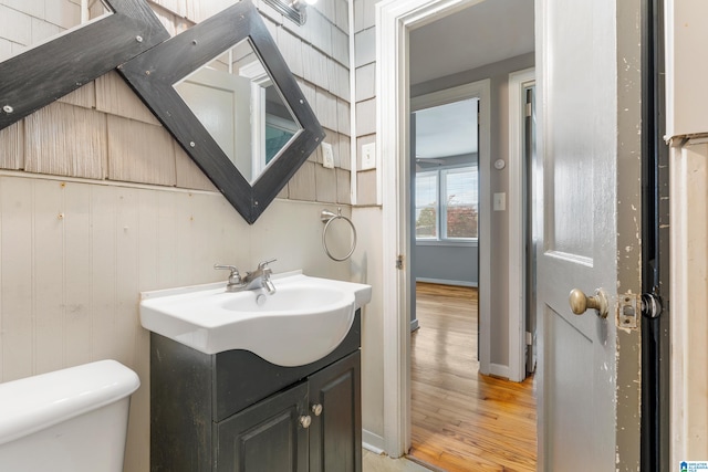 bathroom featuring hardwood / wood-style flooring, vanity, toilet, and wooden walls