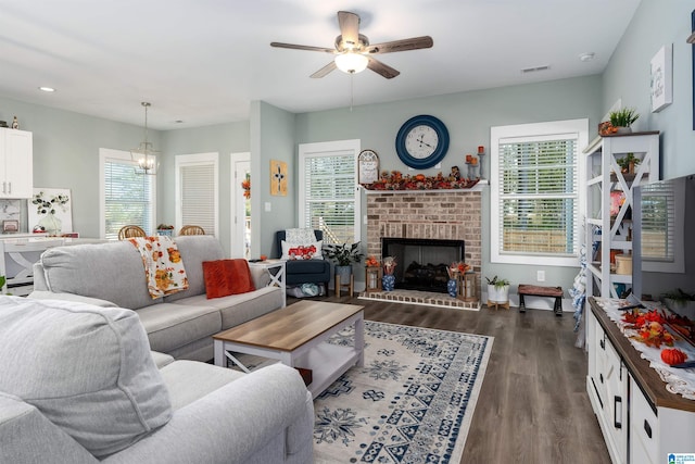 living room featuring a fireplace, ceiling fan with notable chandelier, plenty of natural light, and dark wood-type flooring