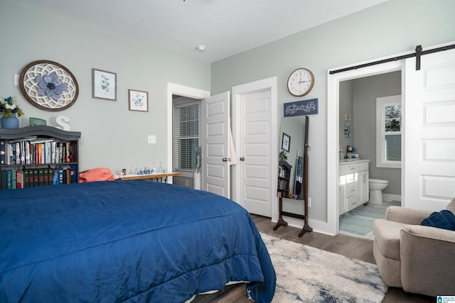 bedroom with a barn door, wood-type flooring, and connected bathroom