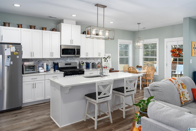 kitchen with appliances with stainless steel finishes, sink, a center island with sink, white cabinets, and hanging light fixtures